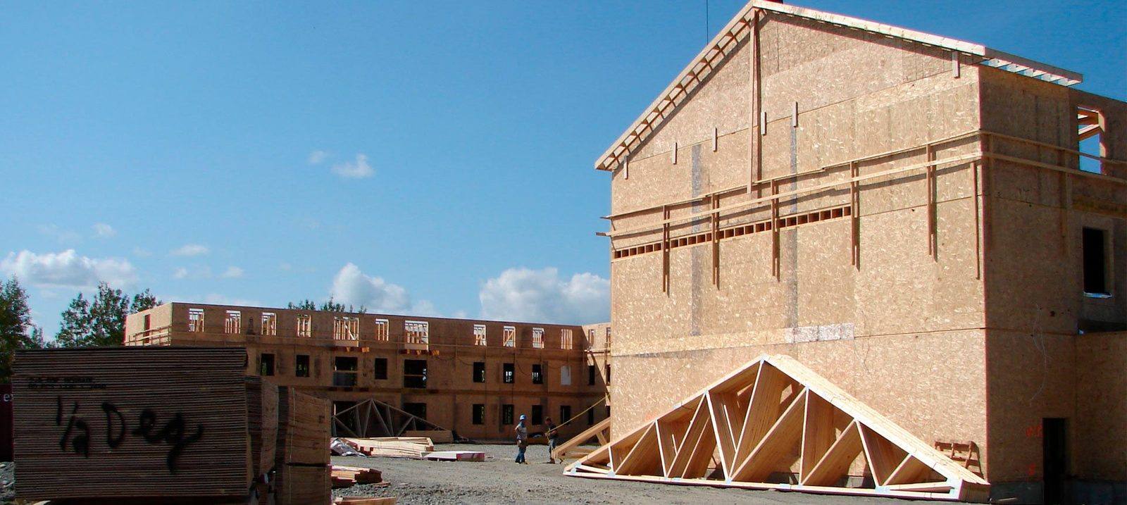 Un mur en panneaux levé à la grue sur un chantier, devant un immeuble à logements en construction