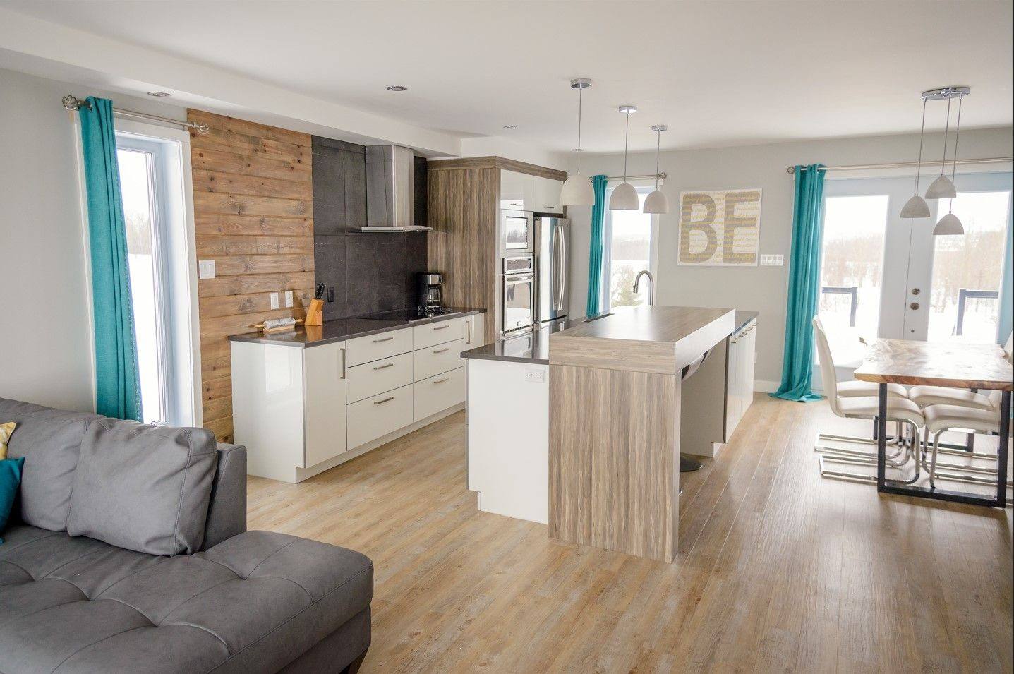 Aire ouverte d'une maison Maison Nordique : cuisine blanche avec îlot, plancher de bois, salle à manger au fond